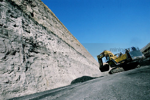 Excavator working next to high walls of open cut coal mine.  coal seam visible. - Mining Photo Stock Library