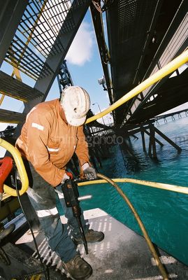 Vertical photo of marine construction worker using a jackhammer to repair wharf pylon.  Full PPE being worn. - Mining Photo Stock Library