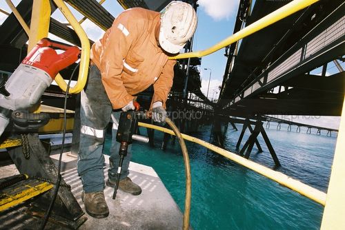 Vertical photo of marine construction worker using a jackhammer to repair wharf pylon.  Full PPE being worn. - Mining Photo Stock Library