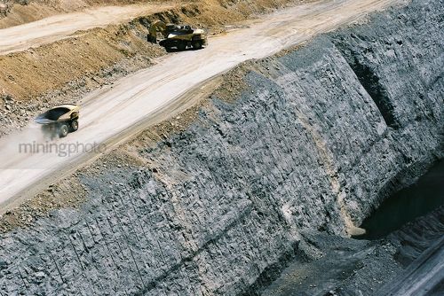 Great aerial phot of haul trucks on access road above coal seam high walls.
excavator working in the background loading haul trucks. - Mining Photo Stock Library