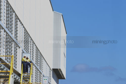 Two mine construction workers taking a break outside plant shed.  blue sky behind.  photo suitable for double page layout. - Mining Photo Stock Library