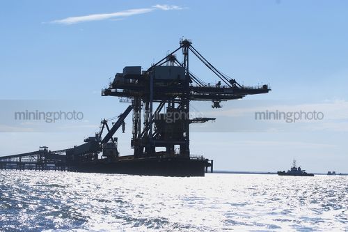 Silhouette of a coal ship loader and wharf with tug boat adjacent. - Mining Photo Stock Library