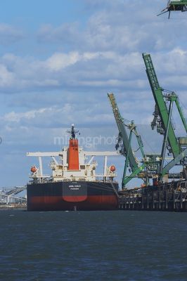 Close up photo of ship loader loading coal into ship at wharf.  vertical shot from water level behind the ship. - Mining Photo Stock Library