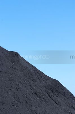 Close up photo of coal stockpile.  blue sky behind. - Mining Photo Stock Library