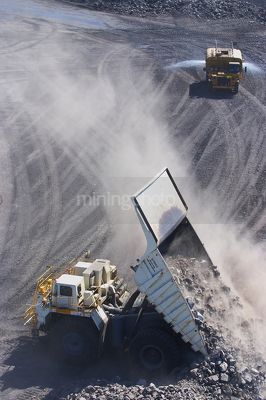 Aerial photo of haul truck dumping overburden at dump site in open cut mine.  watrer cart sprying road in background for dust suppression. - Mining Photo Stock Library