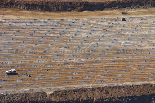Aerial photo of blast worker loading shot holes at open cut mine site.  hundreds of blast hole patterns all around. - Mining Photo Stock Library