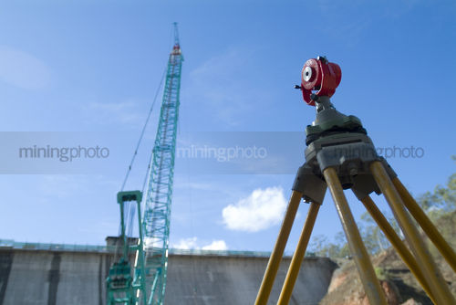 Surveyors survey tool on dam construction site with travel crane in background. - Mining Photo Stock Library