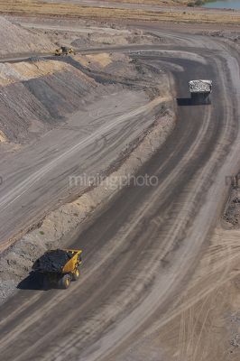 Loaded haul truck with coal following haul truck with overburden in open cut coal mine.  aerial portrait shot. - Mining Photo Stock Library