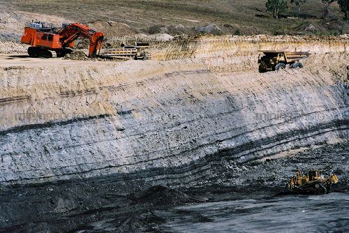 Bulldozer stockpiling coal opencut mine floor while excavator loads haul trucks with overburden on bench above coal seam. - Mining Photo Stock Library