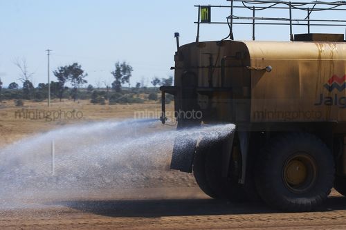 Close up of photo of the rear of a water cart spraying water on haul road in open cut mine. - Mining Photo Stock Library