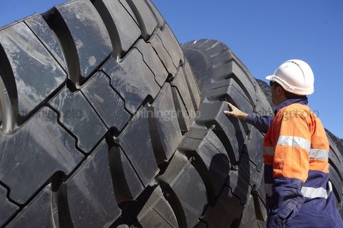 Mine worker in full PPE inspecting truck tyre stockpile. - Mining Photo Stock Library