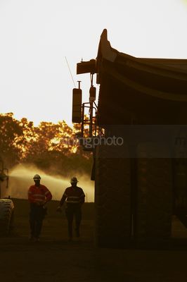 Two 2 workers finishing night shift driving haul trucks walk back to crib room.  workers are in Silhouette with dawn light behind. great teamwork image. - Mining Photo Stock Library