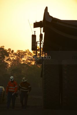 Two 2 workers finishing night shift driving haul trucks walk back to crib room.  workers are in Silhouette with dawn light behind. great teamwork image. - Mining Photo Stock Library