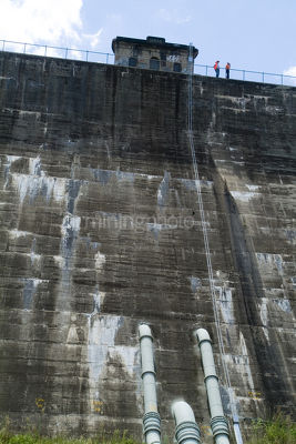 2 workers standing on top of dam wall.  shot from below dam in vertical format - Mining Photo Stock Library