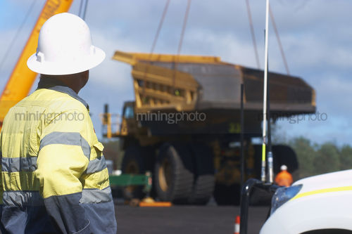Haul truck tray bering lifted by a crane off the back of a haul truck at a mine site workshop.  worker in full PPE observing. - Mining Photo Stock Library