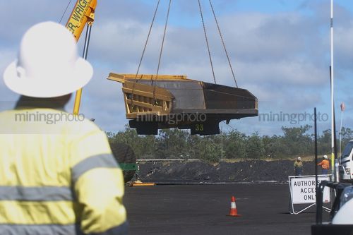 Mine site haul truck tray suspended by crane in workshop area.  worker in full PPE looking on. - Mining Photo Stock Library
