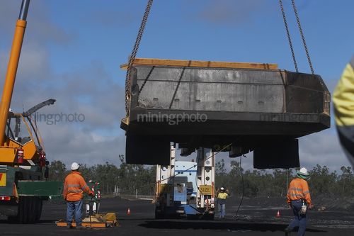 Haul truck tray being lifted by a crane onto the semi trailer of a low loader.  mine workers in full PPE observing. - Mining Photo Stock Library
