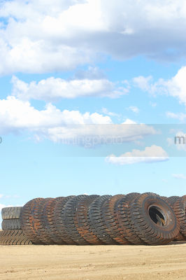 Vertical shot of a truck tyre stockpile of haul trucks at a mine site.  blue sky in the background. - Mining Photo Stock Library