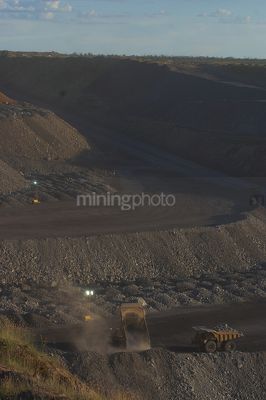 Loaded haul trucks dumping overburden onto the stockpile in an open cut coal mine.  vertical image. - Mining Photo Stock Library