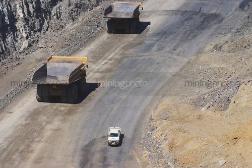 Light vehicle passing two 2 haul trucks on access road in open cut coal mine.  aerial photo. - Mining Photo Stock Library