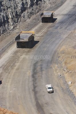 Light vehicle passing two 2 haul trucks on access road in open cut coal mine.  aerial photo. - Mining Photo Stock Library