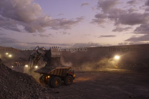 Excavator loading overburden into haul truck in open cut mine.  late afternoon dusk light.  great generic i age that suits a 2 page spread with room for copy. - Mining Photo Stock Library