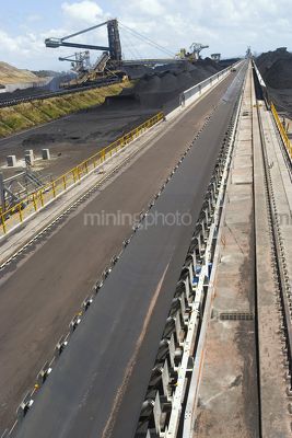 Dramatic photo of a conveyor at coal terminal.  reclaimers and coal stockpiles in background. - Mining Photo Stock Library