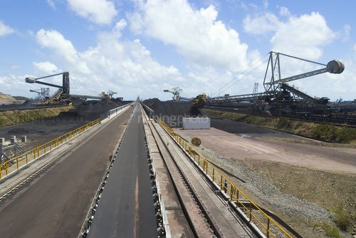 Photo of a conveyor at coal terminal.  reclaimers, coal stockpiles and the port in background, - Mining Photo Stock Library