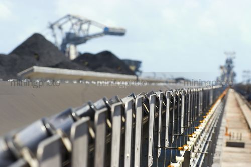 Dramatic shot looking along conveyor to reclaimers and stockpiles at a coal terminal.  selective focus with foreground in focus. - Mining Photo Stock Library