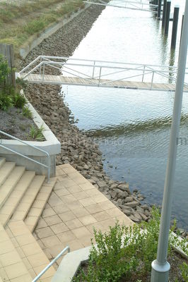 Steps leading down to water in canal property subdivision.  jettys and pedestrian bridges to pontoons in background. - Mining Photo Stock Library