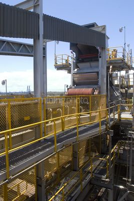 Walkway on multi level coal conveyor at a shipping terminal.  loaded moving coal conveyor in the background. - Mining Photo Stock Library
