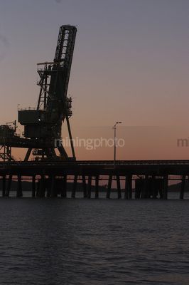 Bulk ship loader at a wharf during sunset.  vertical format. - Mining Photo Stock Library