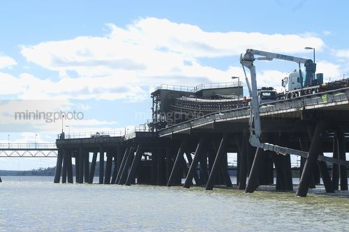 Wharf pylon maintenance workers in travel tower bucket working above water under port access road. - Mining Photo Stock Library