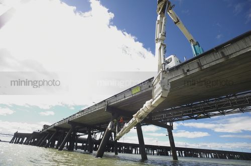 Wharf pylon maintenance workers in travel tower bucket working above water under port access road. - Mining Photo Stock Library