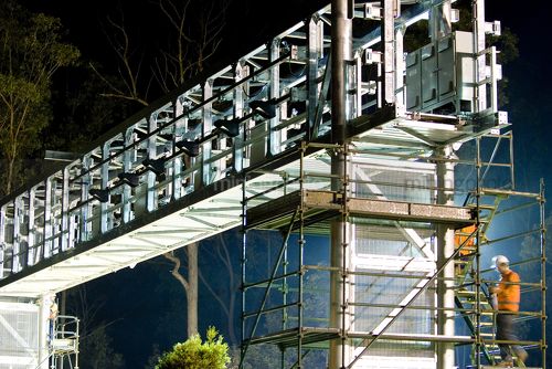 Close up of civil workers on scaffolding in full PPE installing gantry bridge during night time works.  crane holding gantry in place. - Mining Photo Stock Library