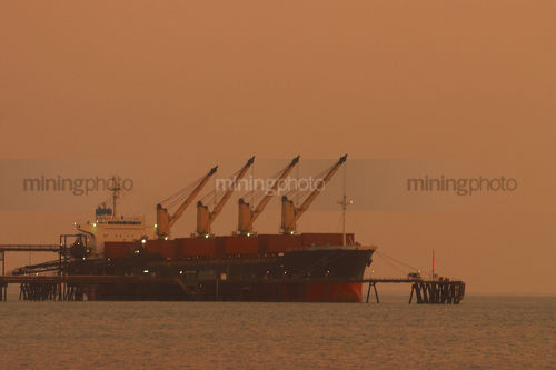 Ship loader loading a berthed ship in early morning light at a wharf. - Mining Photo Stock Library