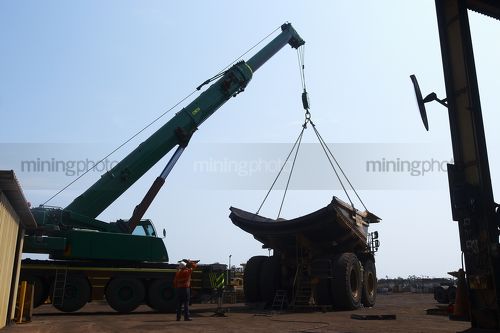 Crane lifting a tray onto a haul truck at the mine site workshop.  worker in full PPE observing.  shot from ground level. - Mining Photo Stock Library