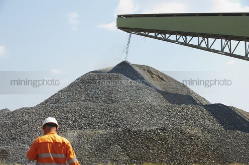 Worker in full PPE with product being stockpiled in background. - Mining Photo Stock Library