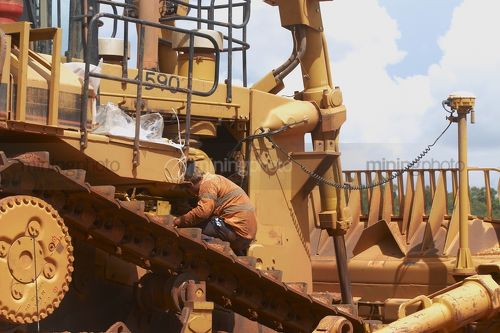 Mine worker servicing a large dozer at a workshop at a mining site. - Mining Photo Stock Library