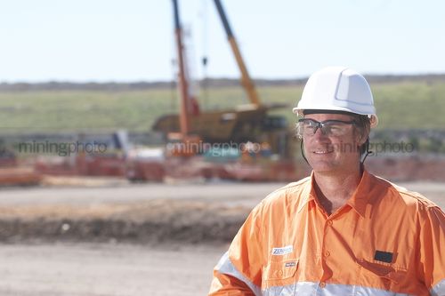 Worker in full PPE looking across the camera near the workshop at a mine site. - Mining Photo Stock Library