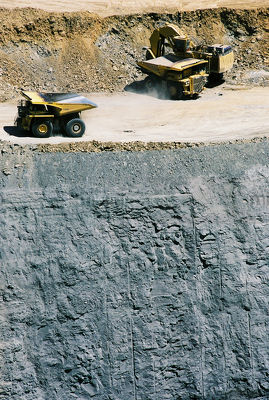 Aerial vertical shot of excavator loading haul trucks in open cut coal mine.  high walls and coal seam below. - Mining Photo Stock Library