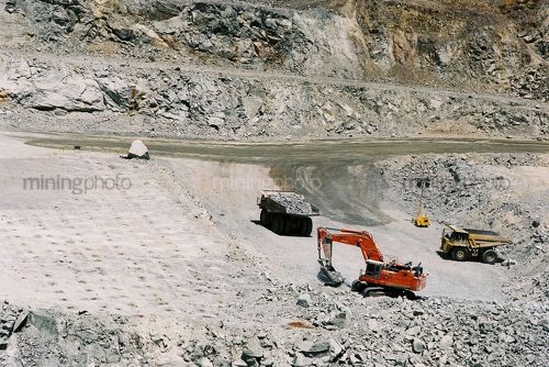 Digger loading product in open cut gold mine.  blast drill holes in foreground. - Mining Photo Stock Library