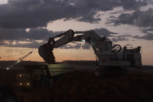 Great dusk shot of excavator loading a haul truck.  generic dusk photo.  machines with lights on. - Mining Photo Stock Library