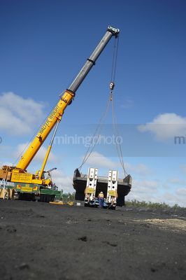 Vertical photo of crane lifting haul truck body of a semi trailer low loader.  blue sky behind. - Mining Photo Stock Library