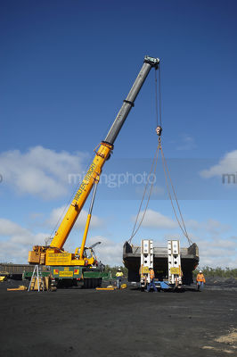 Vertical photo of crane lifting haul truck body of a semi trailer low loader.  blue sky behind. - Mining Photo Stock Library
