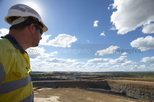 Mine site worker standing on top of open cut coal mine observing the pit.  shot really close with sun backlighting.  great double page layout option. - Mining Photo Stock Library