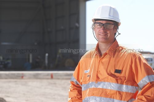 Mine site worker in full PPE looking straight at the camera in front of workshop. room for copy on left hand side. - Mining Photo Stock Library