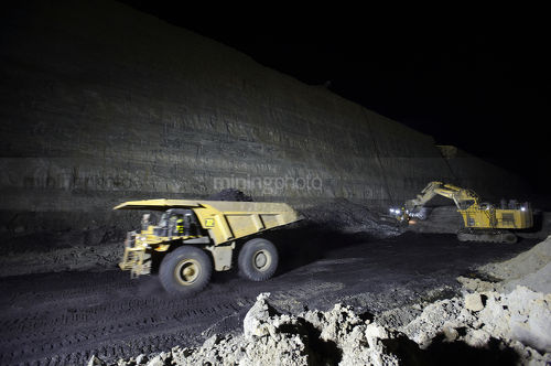 Night time photo of truck and digger in open cut coal mine. loaded truck is moving. high wall and coal seam in background. - Mining Photo Stock Library