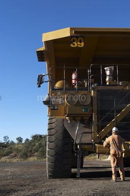 Mine site worker in full PPE  performing maintenance on haul truck at workshop in coal mine. - Mining Photo Stock Library