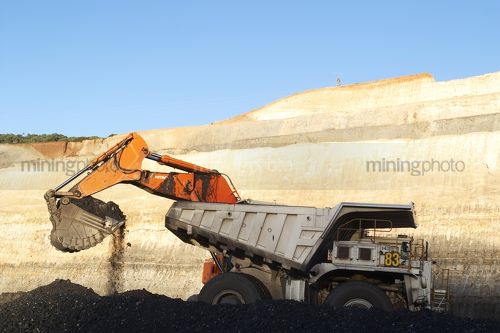 Generic photo of digger bucket loading coal into haul truck in open cut mine.  high walls and coal seam and blue sky in background. - Mining Photo Stock Library